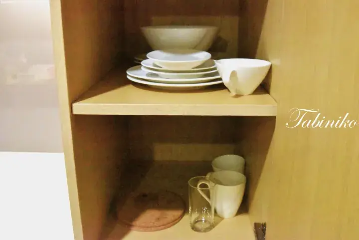 Neatly arranged white ceramic dishes and glassware in a wooden cabinet shelf