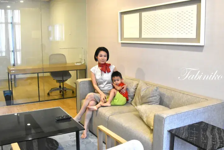 A woman and child sitting on a modern sofa in a bright, stylish living room with glass partitions.