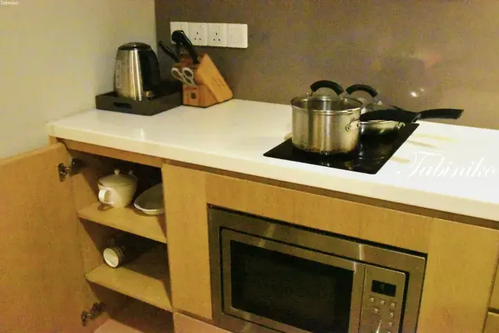 Compact kitchenette with induction cooktop, microwave, kettle, and wooden cabinetry in a serviced apartment.