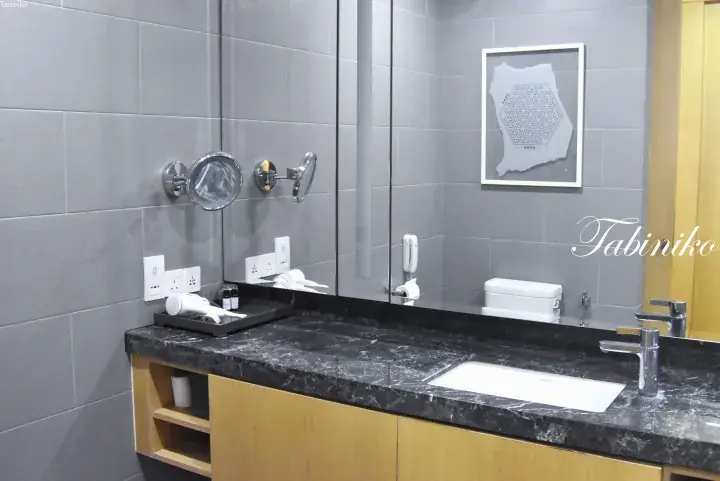 Modern bathroom vanity with black marble countertop, wooden cabinet, and grey tiled walls in a Malaysian property.