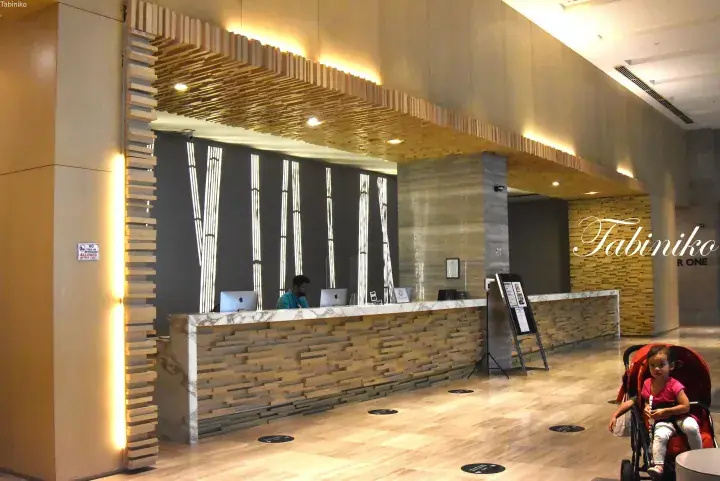 Modern hotel lobby reception with bamboo-themed decor and a guest pushing a stroller.