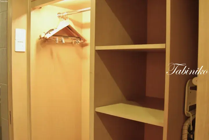 Interior of a modern walk-in closet with wooden shelves and a hanging rod, featuring a Tabiniko watermark.