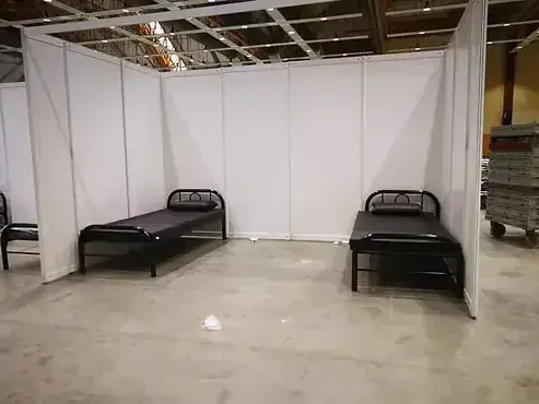Two black metal beds inside a white partitioned room at a warehouse event space.