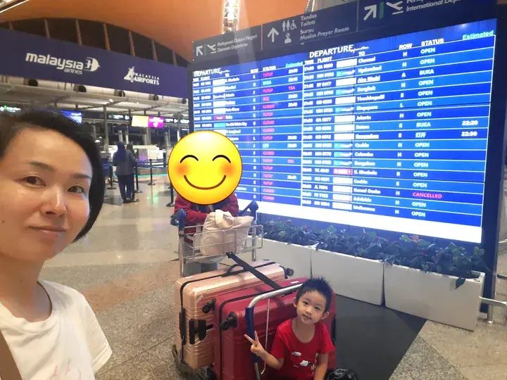 Woman and child at Kuala Lumpur International Airport near Malaysia Airlines check-in counters and a departure board.