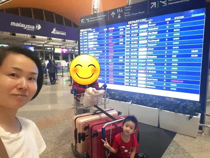 吉隆坡國際機場內,一名女子和小孩站在馬來西亞航空值機櫃台和航班資訊顯示屏前。