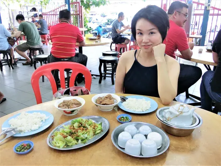 Woman dining at a Malaysian kopitiam with rice, meat soup, vegetables, and tea.