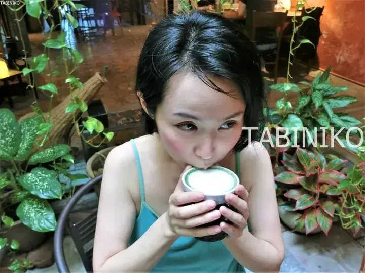 Woman sipping matcha latte in a lush, plant-filled cafe setting.