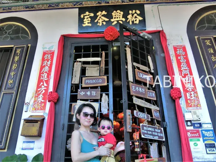 マラッカの裕興茶室の入り口で、ピンクのサングラスをかけた子供を抱く女性。