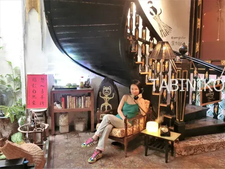 Woman sitting in a vintage chair at Black & White Cafe, surrounded by eclectic decor and a spiral staircase.