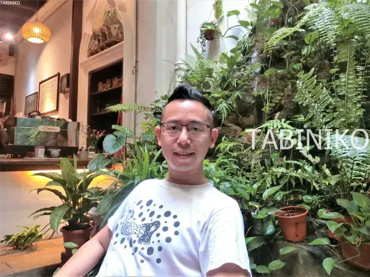 Man in a white t-shirt smiling in a lush cafe with a green living wall and La Cimbali coffee machine.