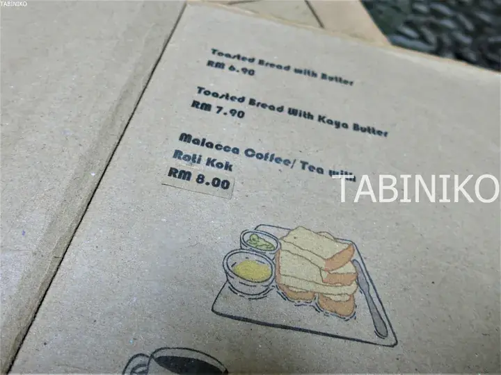 バターパン、カレーパン、マラッカコーヒーとロティコックの価格が記載されたマレーシアのカフェのメニューカード。