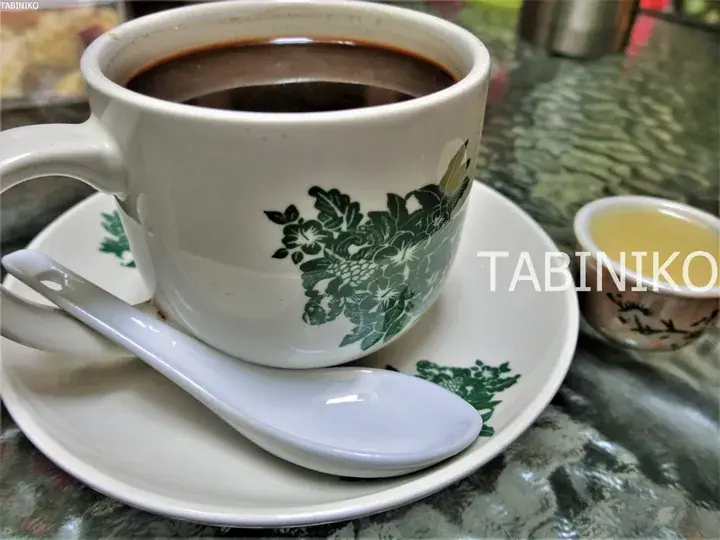 緑の植物柄が描かれた白いカップに入ったコーヒーと、コンデンスミルクが入った小さなボウル。