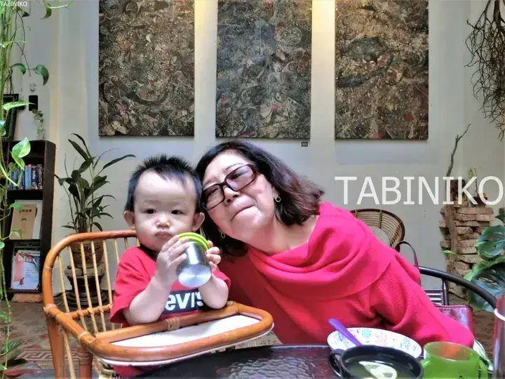 A woman and toddler in matching red outfits sit together at a table in a cozy cafe with abstract wall art.