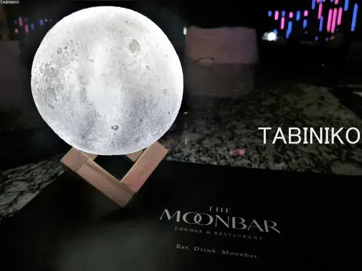 Glowing moon lamp on wooden stand beside The Moonbar Lounge & Restaurant menu.