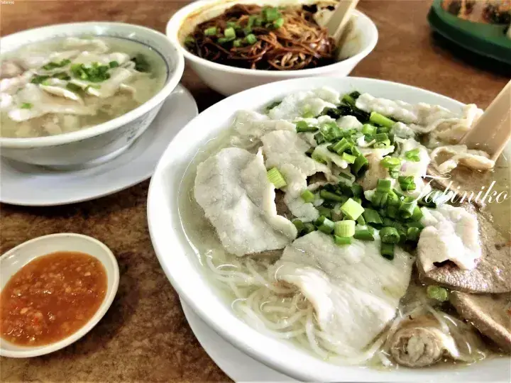 A bowl of pork slice noodles with liver and intestines, accompanied by chili sauce and other dishes.