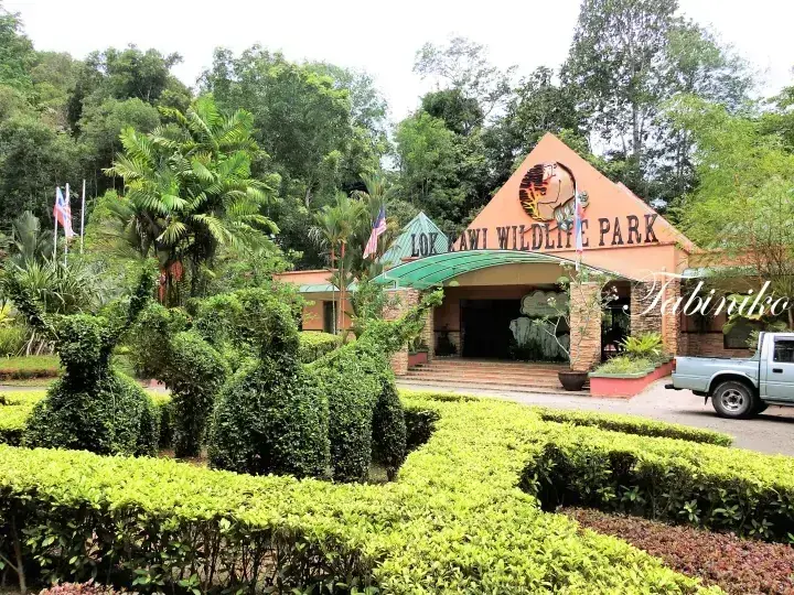 Lok Kawi Wildlife Park entrance building with orange facade and green roof surrounded by lush tropical gardens.