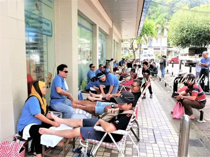 Volunteers in blue shirts provide foot massages to residents outside a building in Labiniko, Malaysia.