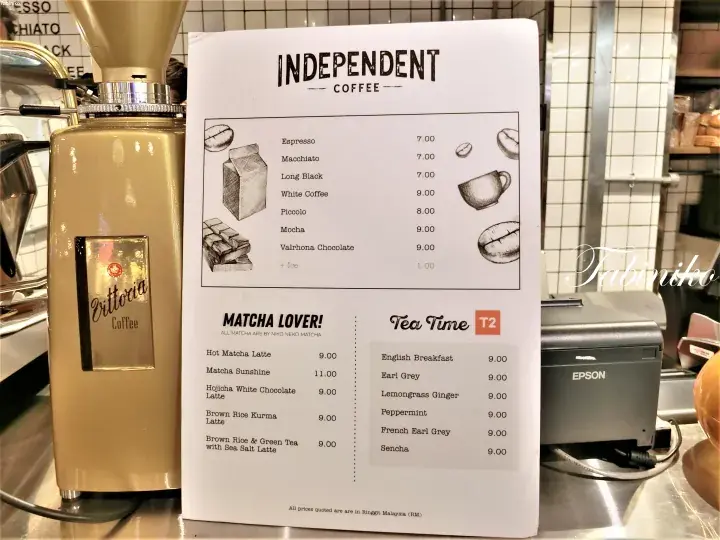 Menu board at Independent Coffee displaying coffee, matcha, and tea options next to a cream Ottavia coffee grinder.