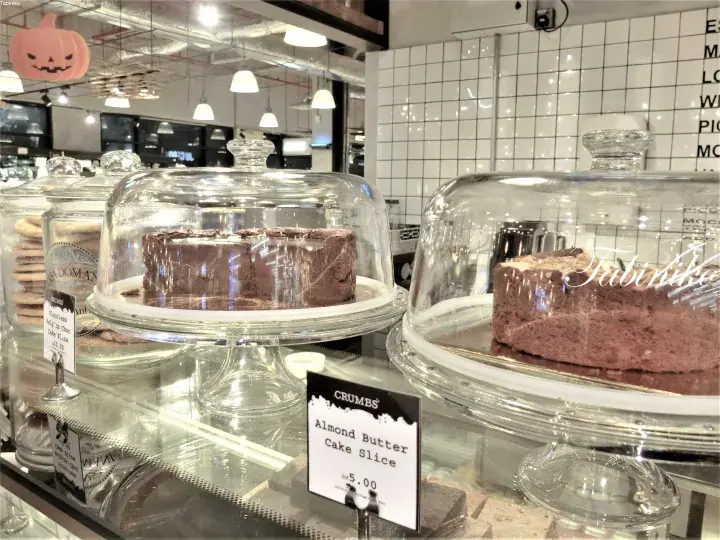 Chocolate and almond butter cake slices displayed under glass domes at a bakery counter.