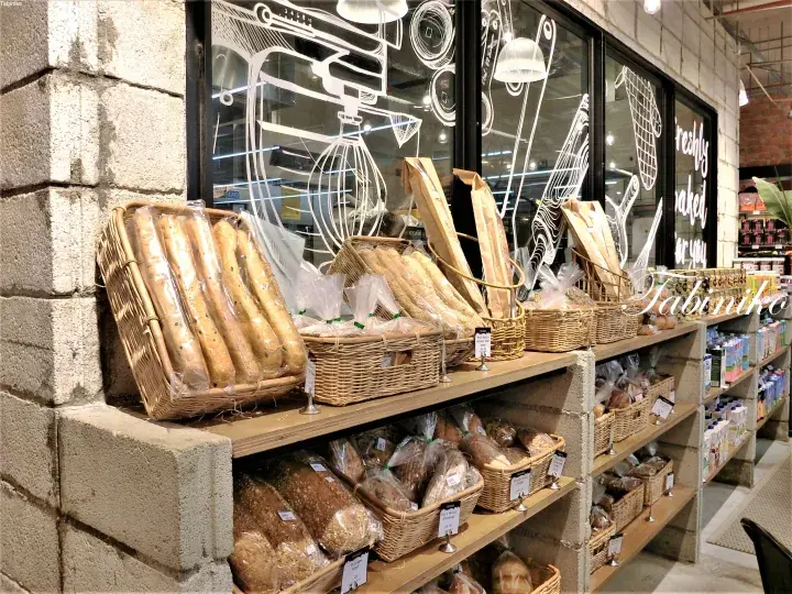 Freshly baked baguettes and artisan breads displayed in woven baskets on wooden shelves at a bakery.