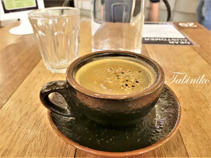 A ceramic cup of frothy coffee on a wooden table with a glass of water in a cafe setting.