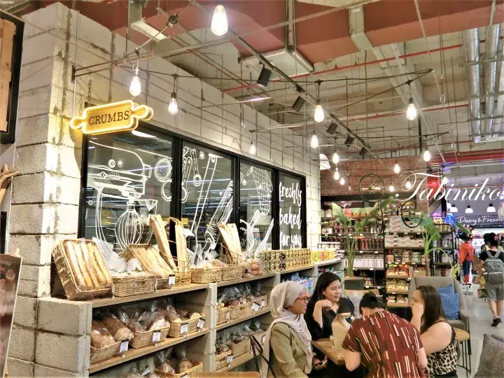 Customers dining near the Crumbs bakery display inside a modern shopping mall with industrial ceiling design.