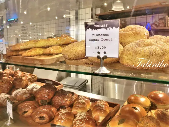 Crumbs Bakery & Cafe display case featuring Cinnamon Sugar Donuts priced at RM3.00 alongside various pastries.