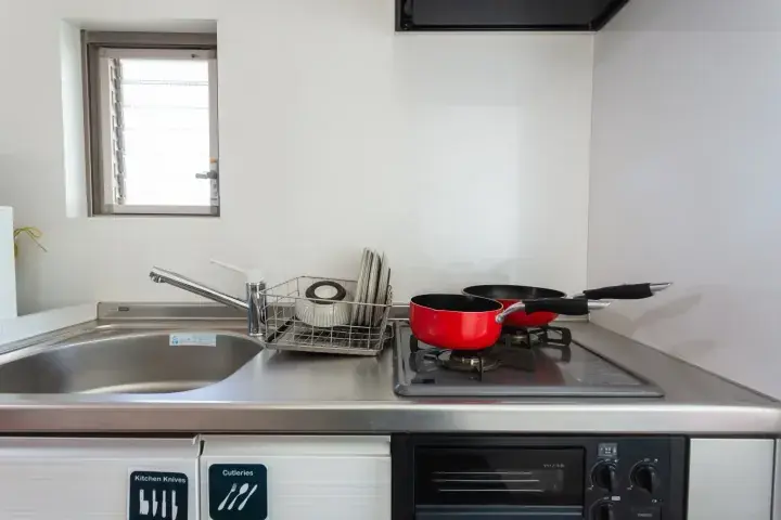 Modern kitchen with stainless steel sink, dish rack, red pots on gas stove, and built-in oven.