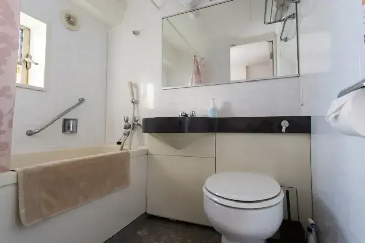 手すりや大きな鏡を備えた、バスタブとシンク、トイレがコンパクトに配置されたモダンなバスルーム。