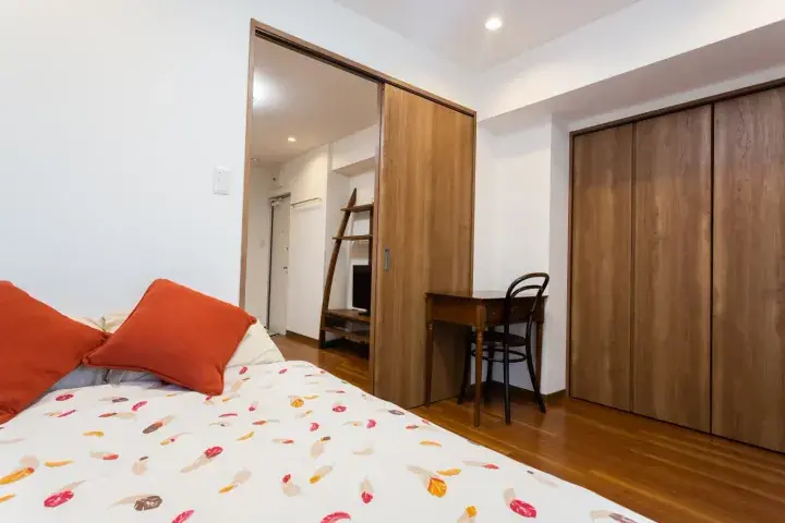 Cozy bedroom with wooden sliding doors, a desk, and a bed with orange pillows and a floral duvet.