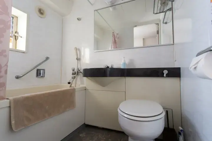 Modern compact bathroom with a bathtub, sink, and toilet featuring a large mirror and grab bar.
