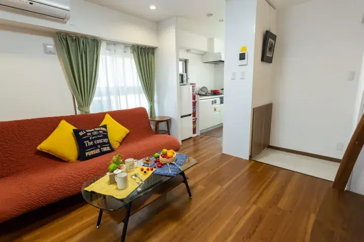 Bright living room with orange sofa, coffee table with fruit, and open kitchen in a modern apartment