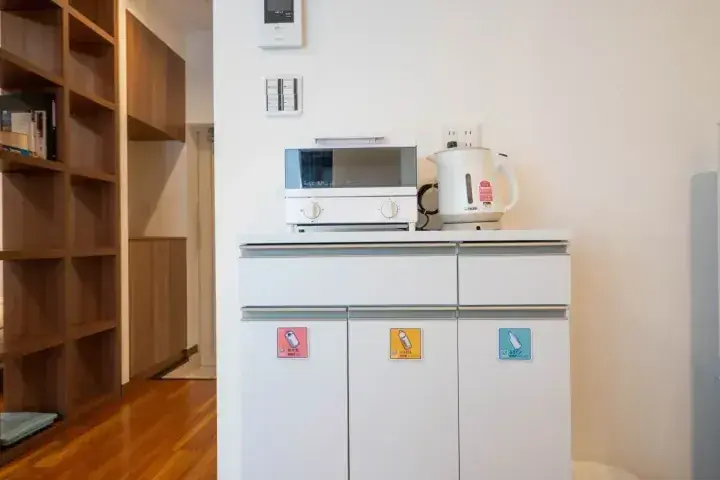 電子レンジとケトルが置かれた白いキッチンキャビネット、背景には木製棚。