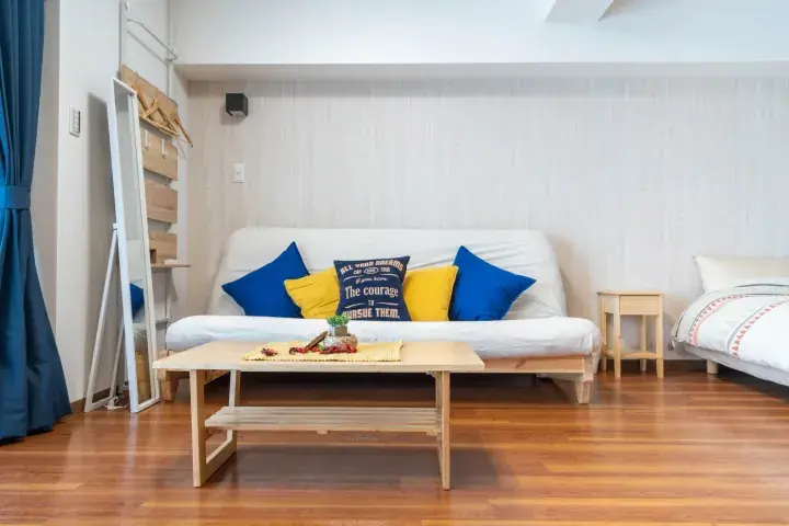 Bright living room with wooden floor, white sofa, blue and yellow cushions, and coffee table.
