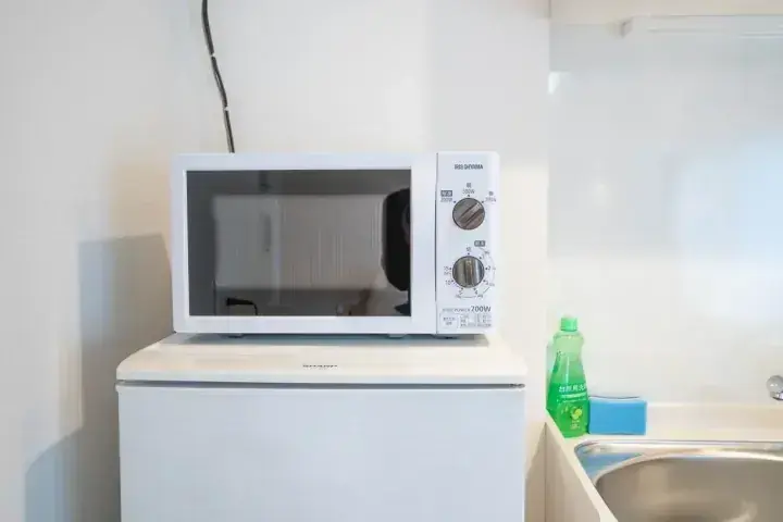 コンパクトなキッチンの白い冷蔵庫の上に置かれたシャープの電子レンジ。