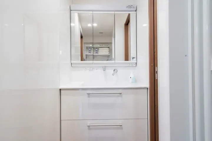 Modern white bathroom vanity with a mirrored medicine cabinet and sleek silver handles.