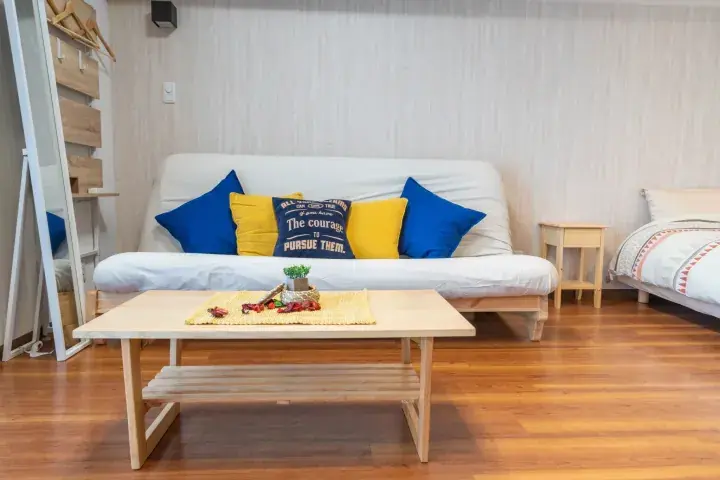 Bright living room with white sofa, blue and yellow cushions, wooden coffee table, and hardwood floors