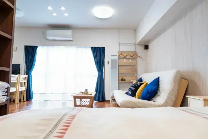 大きな窓と青いカーテン、木製家具が特徴的な明るくモダンなアパートの室内。