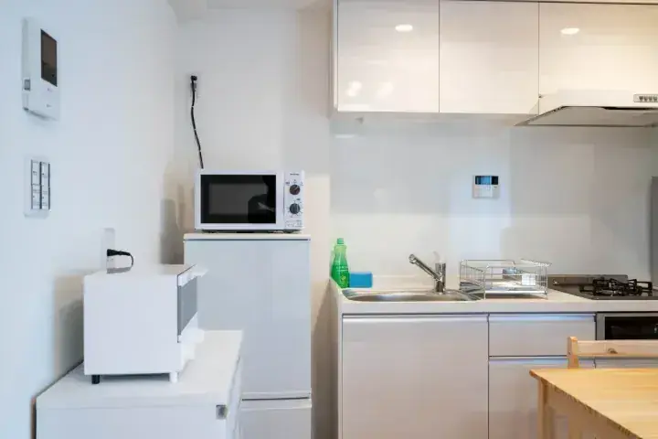 電子レンジやシンク、木製テーブルを備えたモダンな白いキッチンの室内。