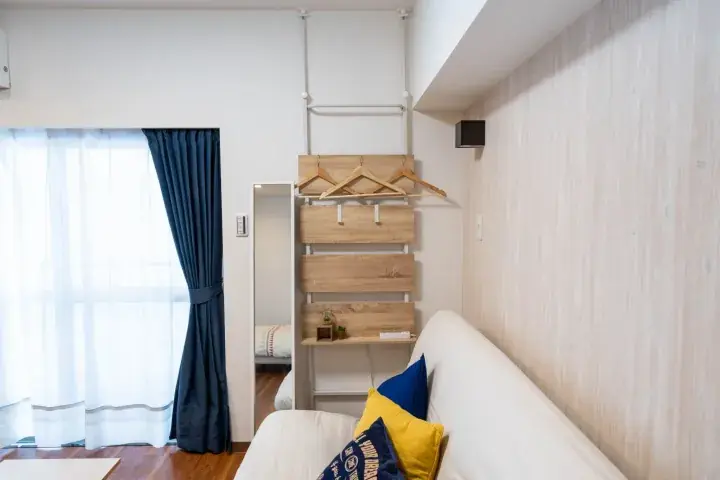 Modern living room with white sofa, blue and yellow cushions, wooden wall rack, and navy curtains.