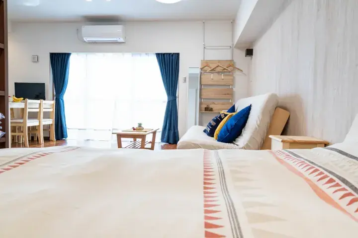 Bright bedroom with patterned bedding, blue curtains, and a wooden dining table near a large window.
