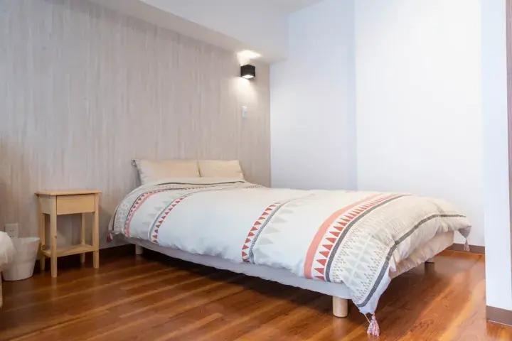 Bright bedroom with wooden flooring, a double bed with patterned bedding, and a minimalist bedside table.