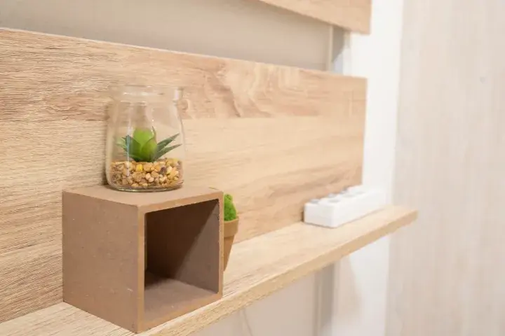 A glass terrarium with a succulent sits on a wooden block shelf against a light wood-paneled wall.