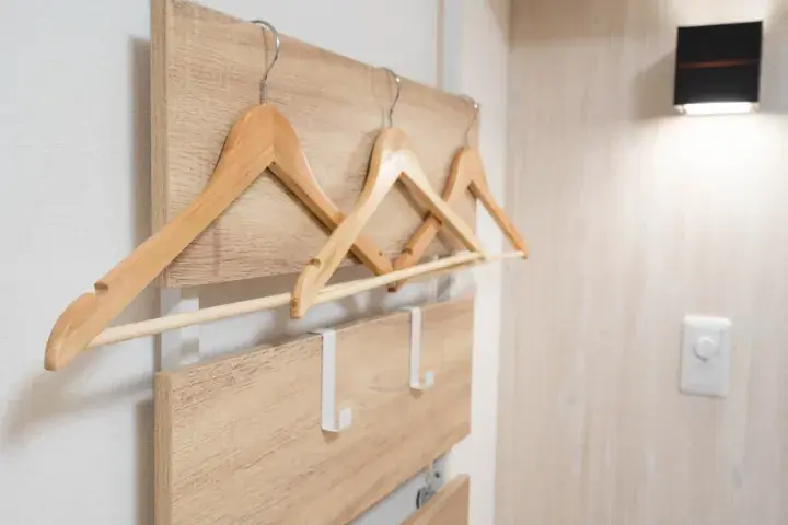 Wooden coat rack with hangers mounted on a wall in a modern property hallway.