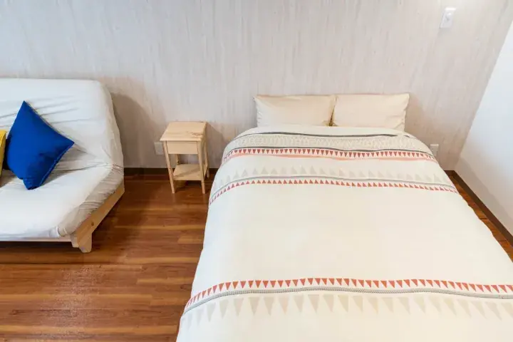 Bright bedroom with a neatly made bed featuring a patterned duvet and a white sofa with a blue cushion.