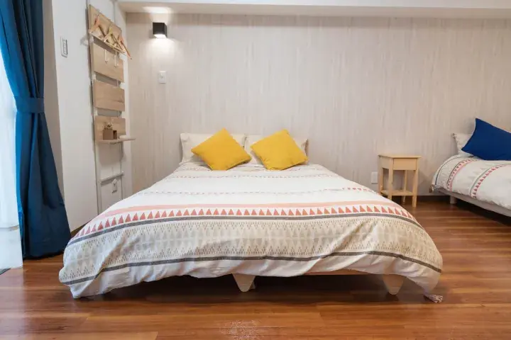 Bright bedroom with wooden floors, a double bed with yellow pillows, and a single bed with a blue pillow.