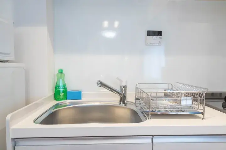 Modern kitchen sink with chrome faucet, dish rack, and green dish soap on a white countertop.