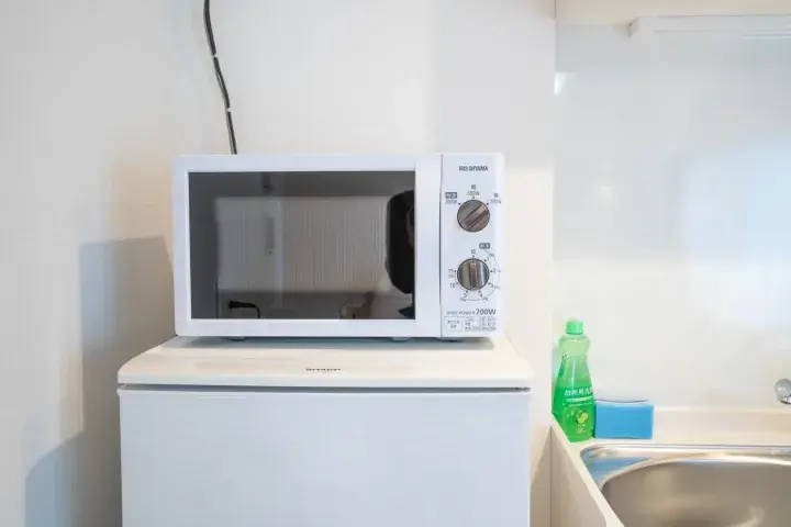 White Sharp microwave oven placed on top of a small white refrigerator in a compact kitchen area.