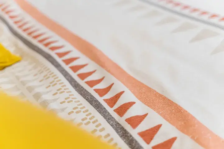Close-up of a bedspread with orange and grey geometric patterns and yellow accents