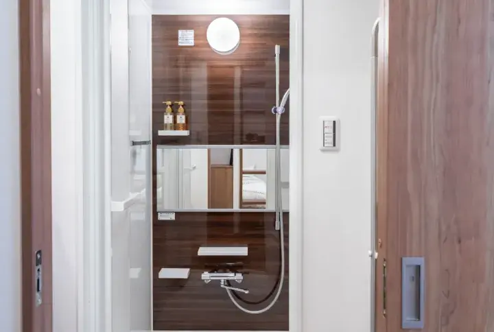 Modern bathroom interior featuring dark wood paneling, a large mirror, and a chrome shower fixture.